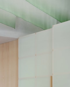 A modern interior space with a wooden wall and glass panels, one with a green tint, creating a warm and natural atmosphere