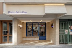 A welcoming coffee shop with a large window, outdoor benches, and a cozy interior seating area with a dining table and chairs