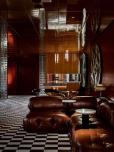 A warm and inviting living space with red walls, brown leather couches, and comfortable seating options, including chairs and dining tables, with wine glasses scattered throughout