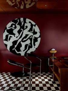 Modern interior space with a red accent wall, black and white circular artwork, two chairs, and a dining table