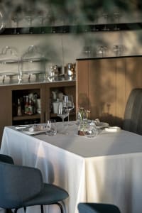 Elegant dining area with a white tablecloth, wine glasses, and dinnerware, surrounded by bottles and two chairs