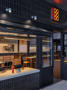 A modern restaurant with black tile walls, multiple dining tables, and chairs, with cups on some tables