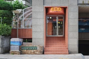 A modern building with a red brick facade, large window, and two doors, set in a contemporary urban environment