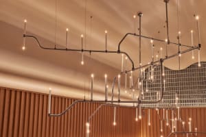 A modern room with a wooden wall, an artistic chandelier, and several candles creating a warm atmosphere