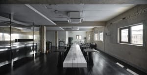 A clean and well-organized dining area with a long white table, multiple chairs, and potted plants, set in a commercial building
