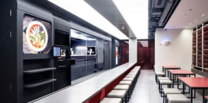 Industrial kitchen with modern black cabinets, red accents, and a long counter with chairs and two TVs mounted on the wall
