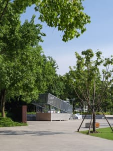 A modern building with a large glass structure in front of it, surrounded by trees, giving a sense of a park or public space