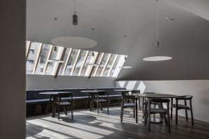 A well-lit restaurant interior with multiple tables, benches, and chairs, featuring natural sunlight and an inviting atmosphere