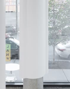 A modern office space with a white column in front of a window, surrounded by parked cars and chairs, conveying a calm and organized atmosphere