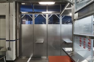Industrial hallway with two stainless steel doors, brightly lit interior, and metal walls