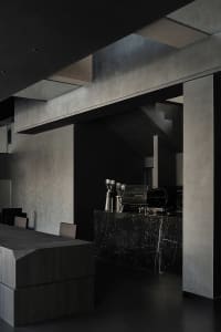 A dark and moody coffee shop interior with a black countertop, coffee machine, and cups, suggesting a nighttime setting