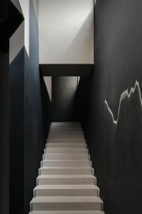 A darkened space with a concrete staircase and black railing, featuring several steps leading upwards