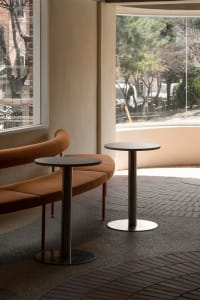 Two orange couches in a well-lit living space with large windows, round tables, and a comfortable atmosphere