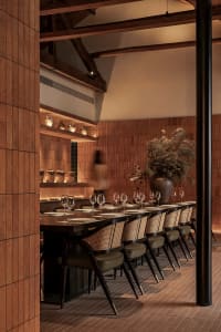 A warm and inviting dining space with a long wooden table surrounded by chairs, wine glasses, bowls, and vases, designed to encourage social interaction among diners