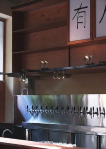 A modern bar area with stainless steel fixtures and a large number of beer taps mounted on the wall in a lively social environment
