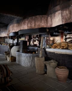 A traditional European-style kitchen with a rustic atmosphere, featuring various food items, bowls, bottles, and apples on tables and counters