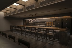 Dimly lit restaurant kitchen with a wooden bar counter and chairs, creating a cozy ambiance
