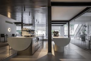 Industrial kitchen with two white sinks, two coffee makers, and three chairs, featuring a clean and organized atmosphere with a focus on functionality and efficiency