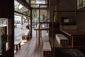 A warm and inviting lobby area with wooden floors and walls, featuring a woman sitting on a bench and several people engaging in activities, with motorcycles parked outside the entrance