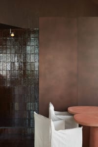 Cozy living space with a brown wall featuring a tile pattern, a dining table, and two chairs, one with a white cushion