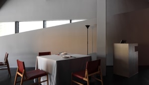 A dining area with two chairs and a tablecloth, featuring a vase and three bowls on a table