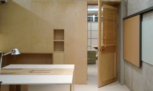 Office space with wooden walls and floors, featuring two desks, chairs, and storage drawers, with a clean and organized atmosphere