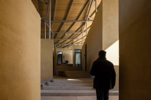 A hallway with concrete walls, featuring steps leading upwards and two people, one near the left side and one further back on the right side