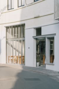 Modern commercial building with a white facade, large windows, a glass door, and a window on its side, set against a neutral background