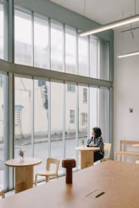 Inviting cafe with concrete walls, large windows, and potted plants, featuring a comfortable seating area with dining tables and chairs