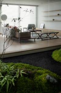Open living area with a couch, chairs, dining table, and potted plants, surrounded by glass walls and natural light