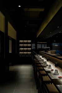 A dimly lit restaurant interior with a long wooden dining table and chairs, set for dinner service