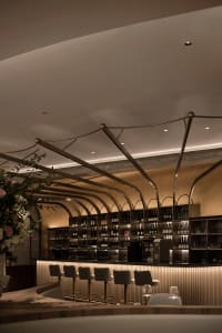 A modern bar area with a stainless steel counter, wine bottles, and comfortable seating, set in a warm and inviting atmosphere