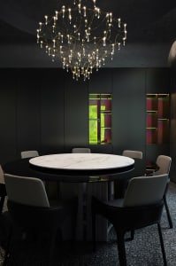 Dining space with a round marble table, four chairs, and a chandelier in a black color scheme