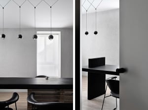 Modern office space with black chairs, a dining table, and a desk near a window, featuring clean lines and minimalistic elements, well-lit with natural light