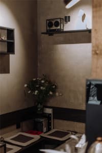 A dimly lit room with a vase of flowers on a table, two speakers, and a TV mounted on the wall, in a minimalist style with a focus on functionality and simplicity