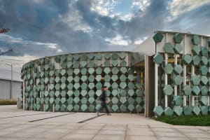 A building with a unique design featuring green tiles on its exterior walls, with two people walking in front of it