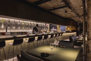 Modern bar area with a long counter, multiple bottles, and seating for patrons