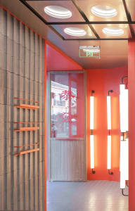 A warm and inviting restaurant entrance with a red doorway, natural light from a window above, and lights on either side