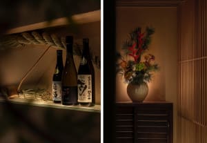 A table with a vase of red flowers and several bottles arranged in a row, creating a cozy and inviting atmosphere