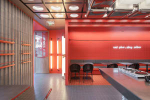 Cozy restaurant dining space with red brick walls, orange accents, and multiple seating options including chairs and benches