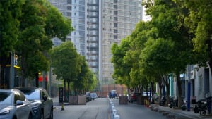 A bustling city street scene with a tall building, trees, cars, motorcycles, and pedestrians