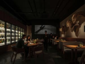 A lively indoor dining space with multiple tables and chairs, featuring people enjoying meals and conversations, with bottles on surfaces
