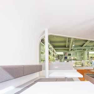 A casual restaurant interior with a large concrete wall, tables, chairs, bottles, and wine glasses, creating a relaxed atmosphere for socializing and dining
