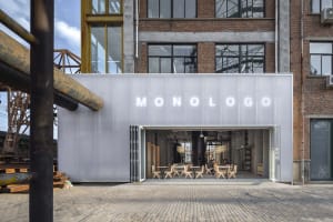 Industrial restaurant space with chairs, a dining table, and concrete walls, lit for a comfortable atmosphere