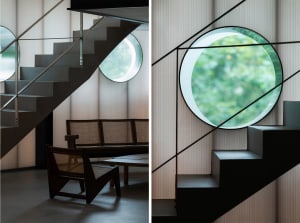 Comfortable living area with chairs and natural light from windows, contrasted by a black staircase railing