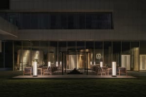 An outdoor dining area with chairs arranged around a table on a grassy surface, set in front of a building at night