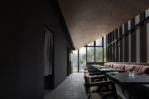 A modern restaurant interior with a large dining table surrounded by chairs, featuring a combination of black and white elements and dim lighting