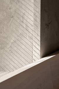 A modern indoor space with a concrete wall and a wooden surface, featuring a shadow cast on the wall, in a bright and well-lit atmosphere