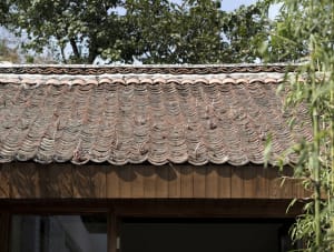 Old building with a tiled roof featuring a combination of wood and tile elements, surrounded by sunlight and a wooden exterior