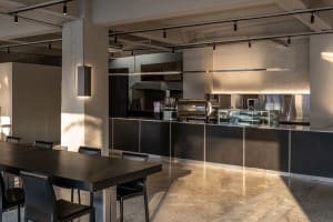 Industrial kitchen with concrete flooring, large countertop, and modern appliances, surrounded by chairs and a dining table